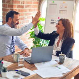 Man and woman high fiving each other in office after successful strategy meeting