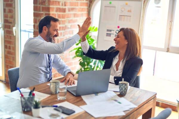 Man and woman high fiving each other in office after successful strategy meeting
